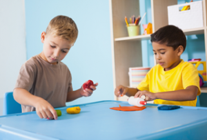 A photo of two boys approximately four to five years old playing with modeling clay in a classroom setting