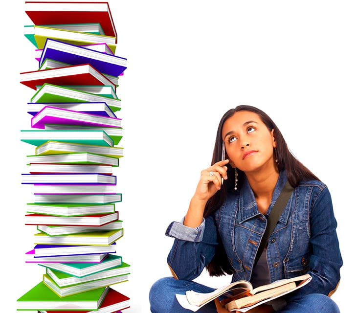 Sophia sits with a pile of schoolwork in her lap, looking up with a frown at a stack of books next to her which is taller than she is.