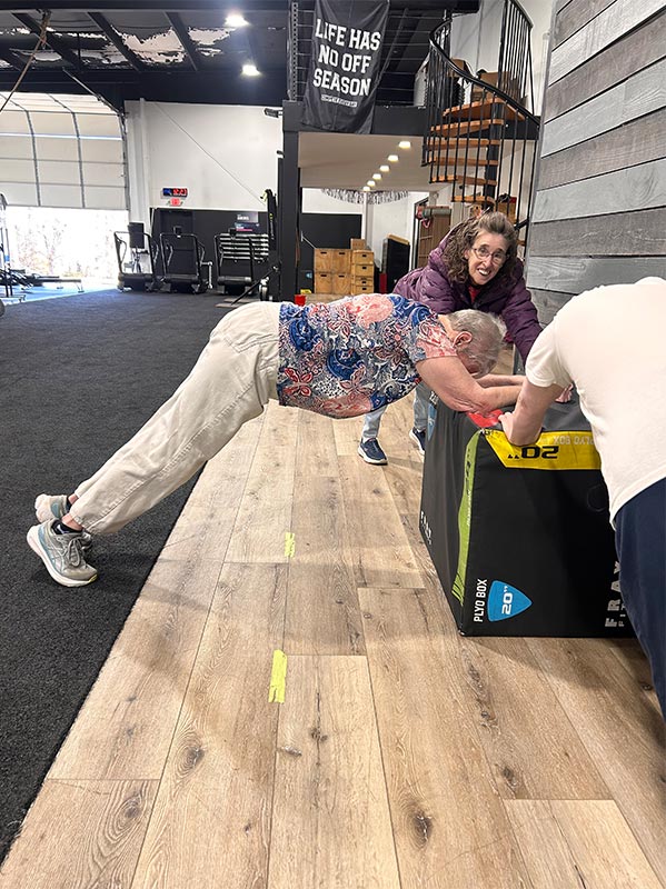 Three people performs a plank on a raised surface, supporting their core while staying off the floor for safety and comfort.