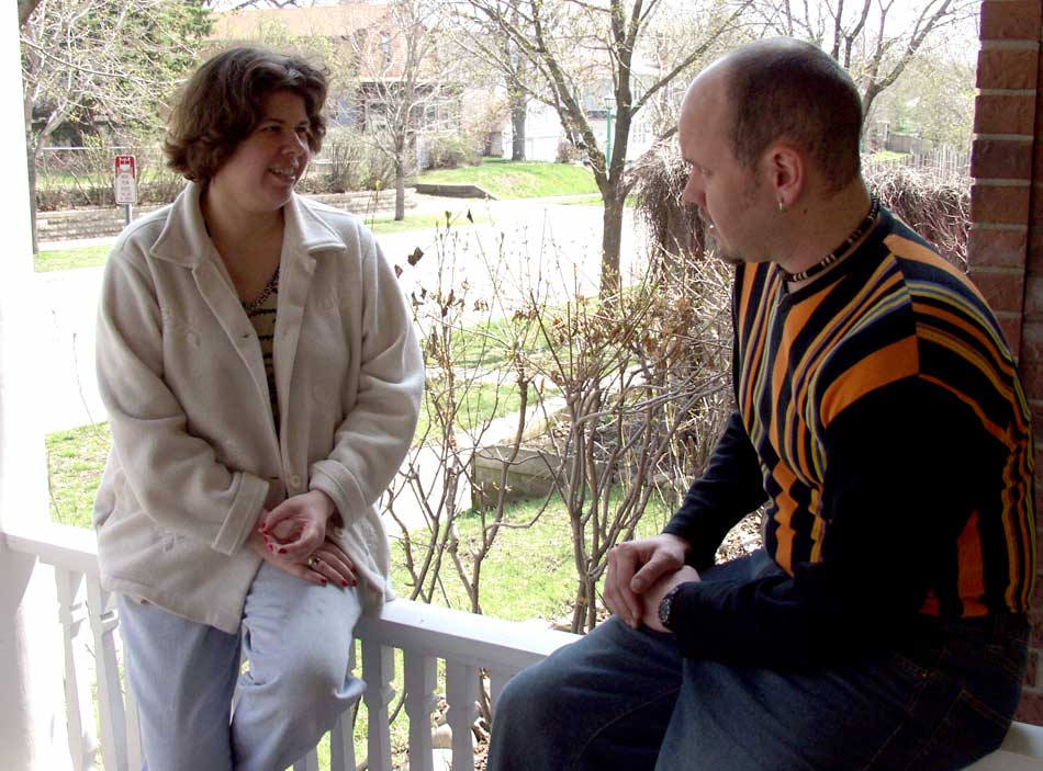 A man and woman sit talking with each other on a porch.