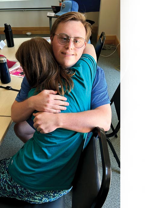 Two people in blue shirts hug each other while sitting at a table.