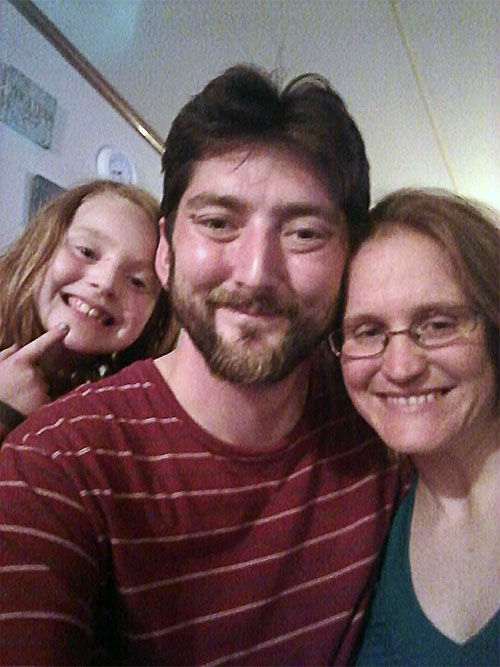 Family of three, blonde girl about 11 years old, man with dark hair, beard and red shirt with white strips, woman, Tasha, brown hair, glasses and dark green top.