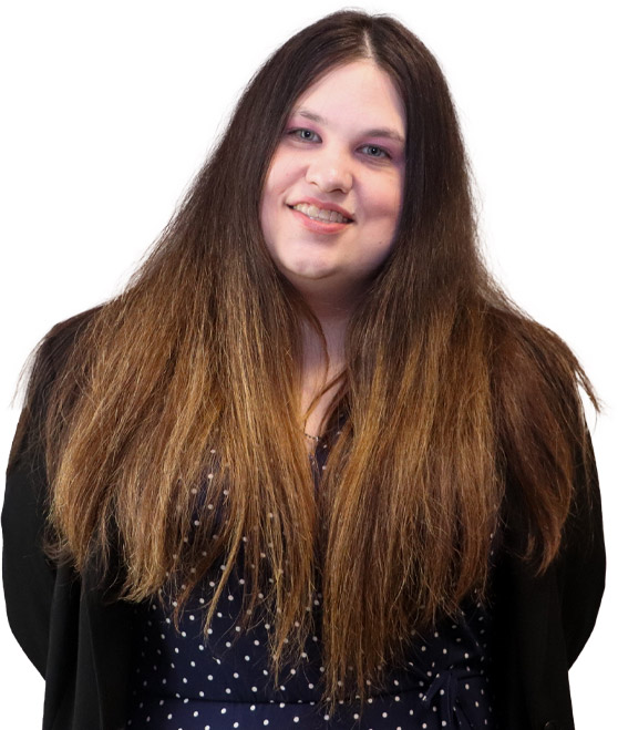 A woman with long, straight brown hair and a dark, polka-dotted shirt smiles as she looks straight ahead.