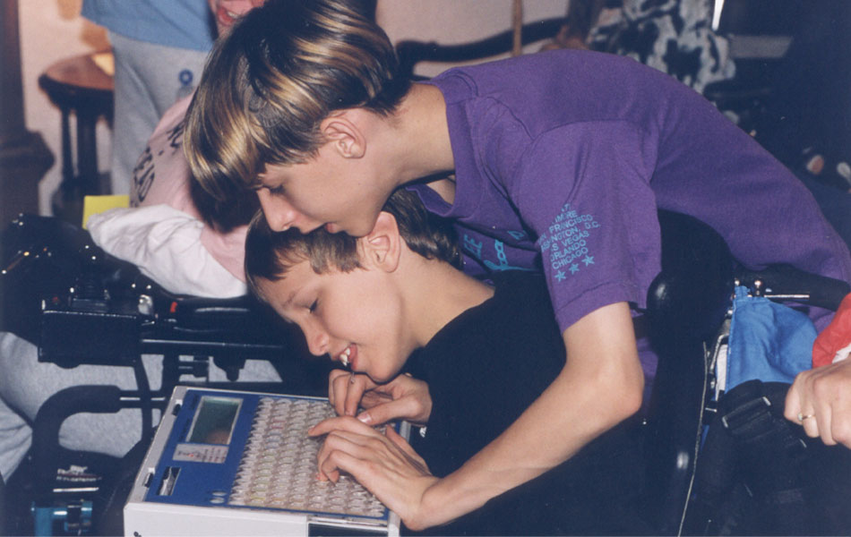 Two boys hunch over an early alternative communication device.