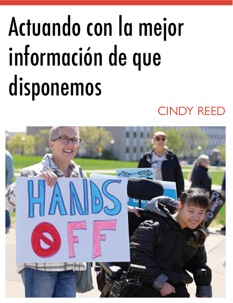 «Actuar con la mejor información de que disponemos», escrito por Cindy Reed. Debajo del titular, hay una fotografía de dos personas al aire libre. La persona de la izquierda tiene la piel clara, el cabello rubio corto y canoso, y lleva gafas, una camisa a cuadros y vaqueros azules. Esta persona sostiene un cartel en el que se lee «HANDS OFF» (No toques) en grandes letras azules y rojas. La persona de la derecha, que utiliza una silla de ruedas eléctrica, tiene la piel clara, el pelo liso y castaño con flequillo, y lleva una chaqueta negra. Ambas personas están sonriendo. Al fondo hay otras personas, algunas con gafas de sol y chaquetas, y el escenario parece ser un exterior en un día soleado, con árboles y edificios visibles.