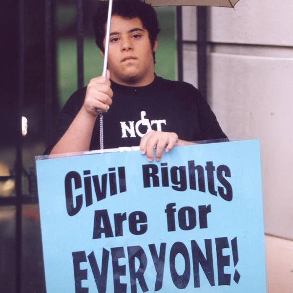 Joven adulto sosteniendo un gran cartel que dice «¡Los derechos civiles son para todos!».
