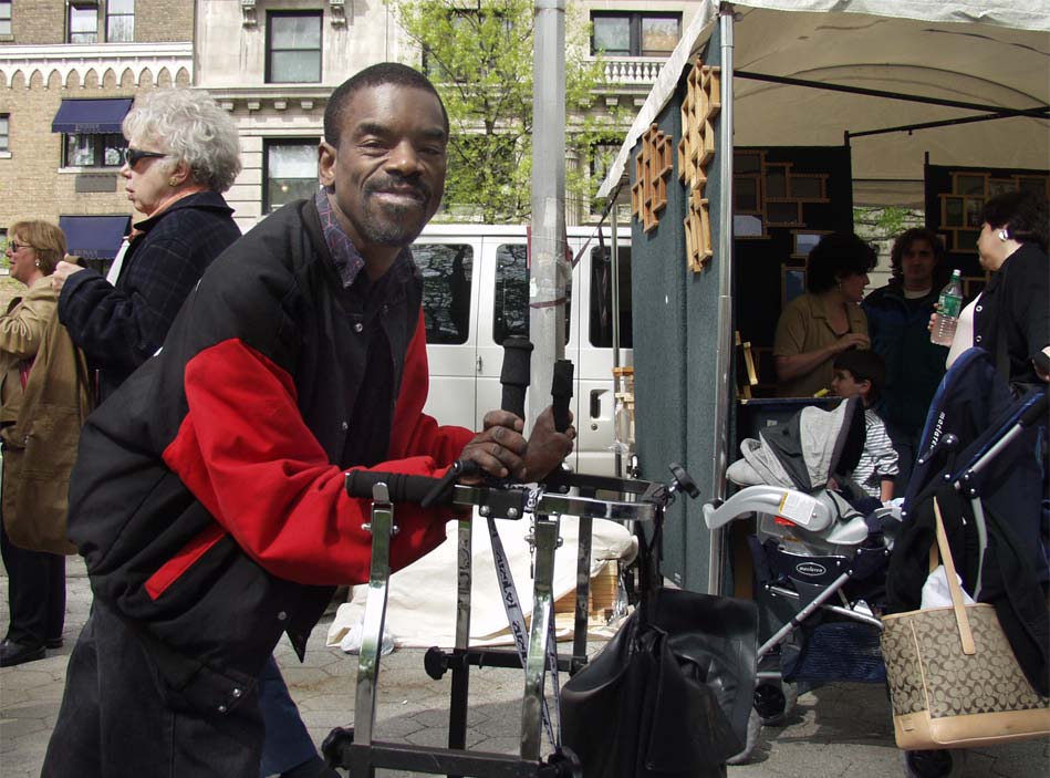 A man wearing a black and red jacket smiles as he stands on a busy street.