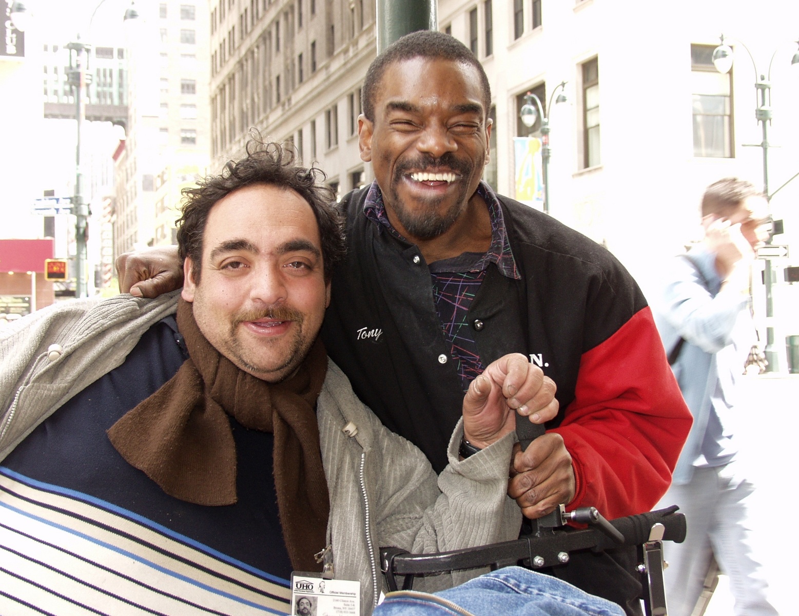 A man with a disability and his direct support professional share a laugh on a city street.