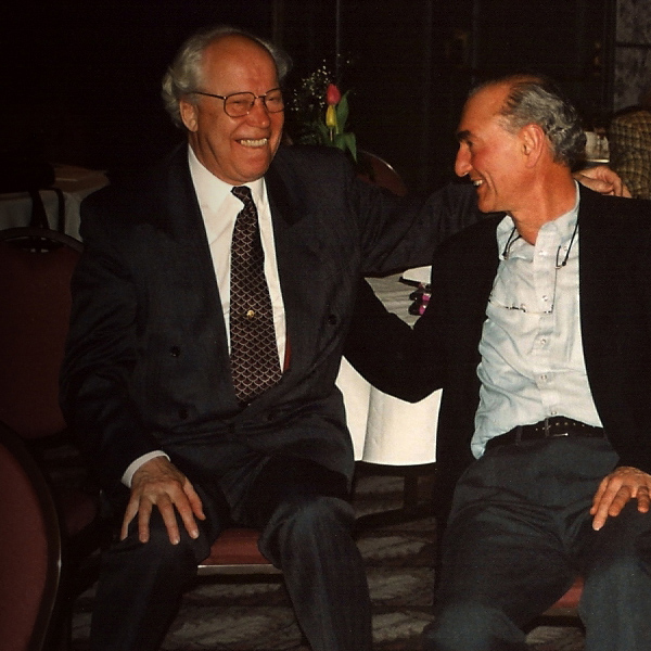 Two older men seated with arms around one another, laughing