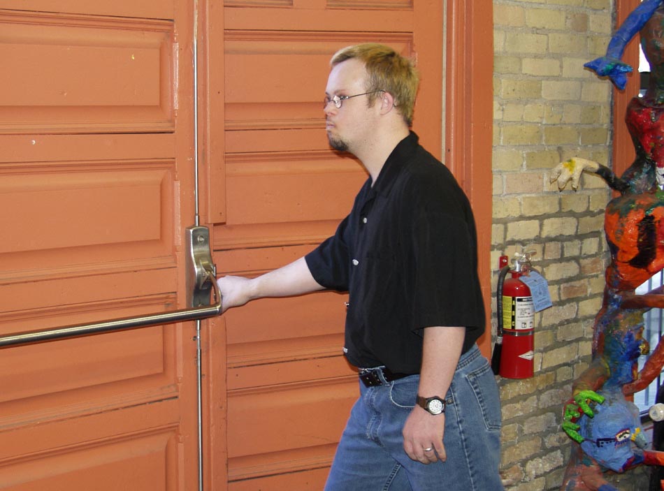 A man wearing a black shirt and jeans reaches to open a door.