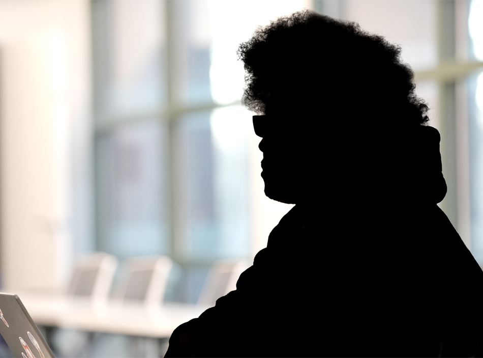 Perfil en sombra de un hombre con un gran afro, sentado a una mesa. El fondo está borroso.