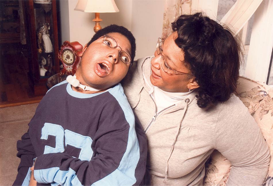 A person with a tracheostomy tube looks into the eyes of an older woman, who is smiling.