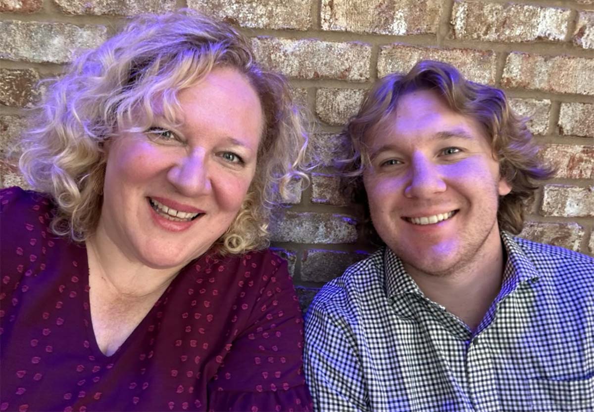 Kim Tarver and Henry Teal are looking at the camera smiling. Kim is on the left. She has curly blonde should-length hair and is wearing a maroon blouse with a small print. Henry has wavy brown hair. He is wearing a black and white small checked button down shirt.