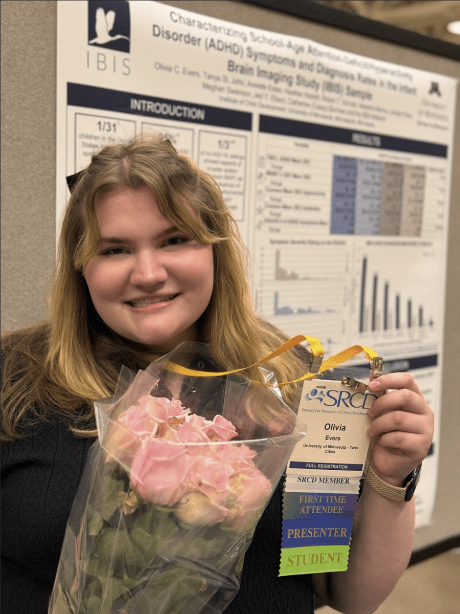 Olivia Evers (MNLEND 2024-25) holds a bouquet of pink roses and her presenter badge. She stands in front of a conference poster she co-authored.