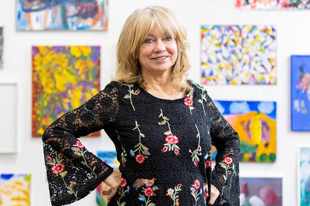 Jeanne Calvit stands in front of modern art paintings in a gallery.