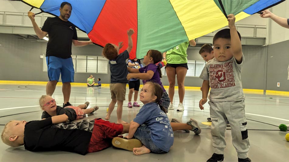 Adultos y niños en edad preescolar juegan a un juego con un paracaídas en un gimnasio