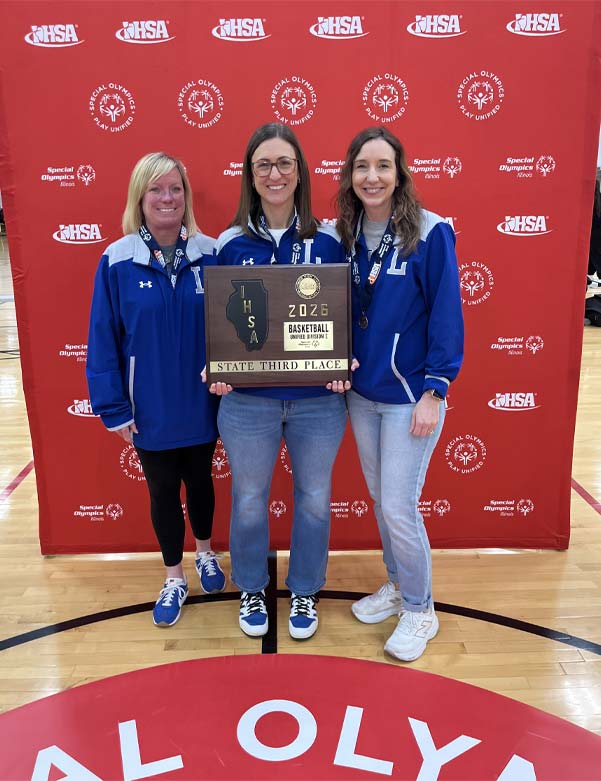 Tres personas de pie junto a una placa en una cancha de baloncesto.