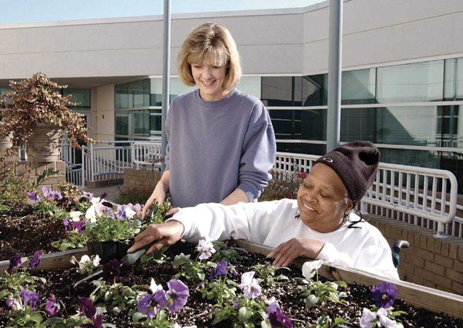 Two women tend a raised flower bed.
