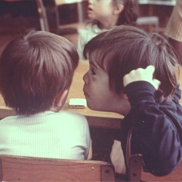 A child with Down syndrome whispers in the ear of a classmate