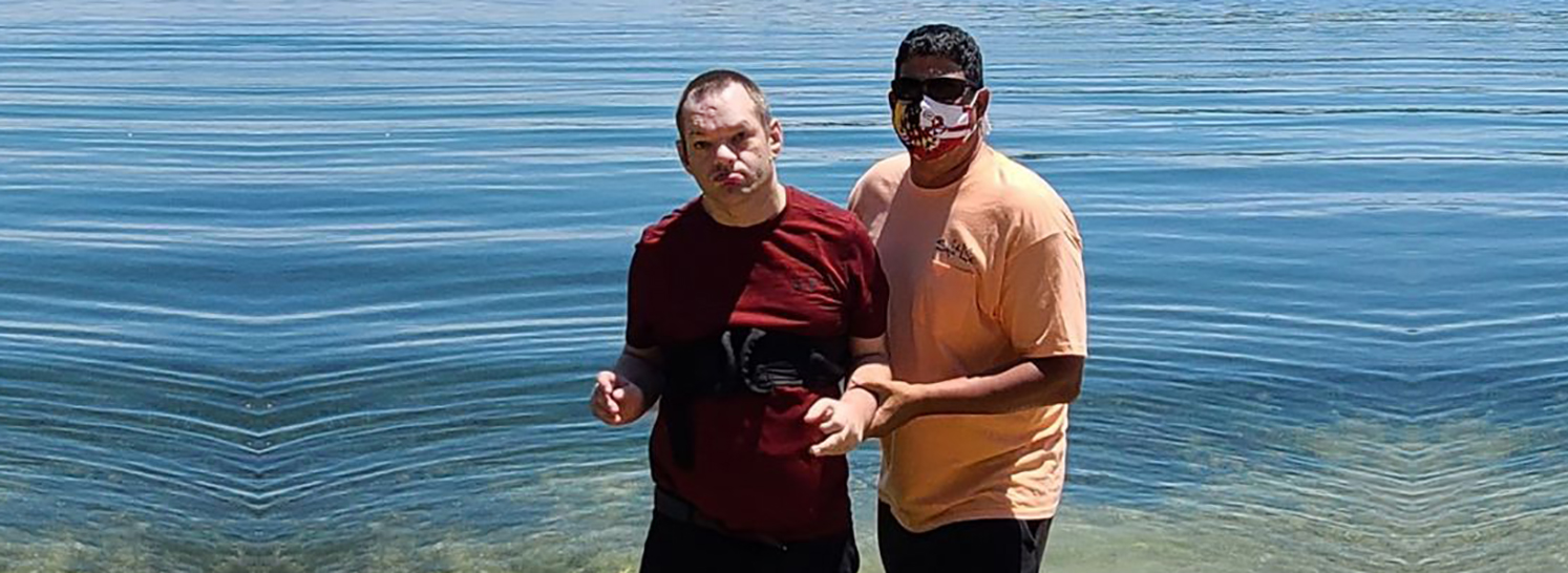 Direct support professional standing with man in front of lake.