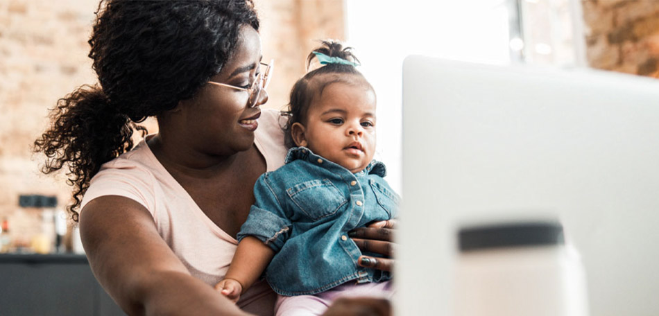 Una mujer mira a un bebé que tiene en su regazo, mientras que el bebé mira la pantalla de una computadora.